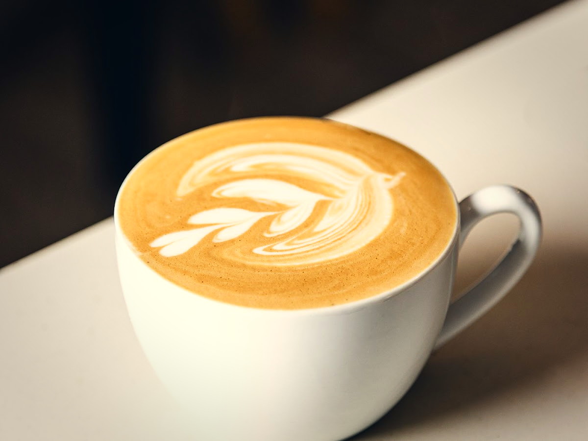 A flat white with latte art in a white cup on a wooden counter