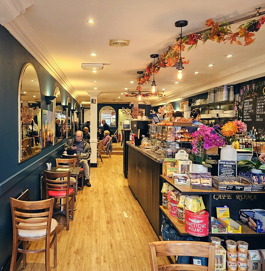 Inside Cafe Roma — teal walls, arched gold mirrors, honey wood floor and the counter at the far end